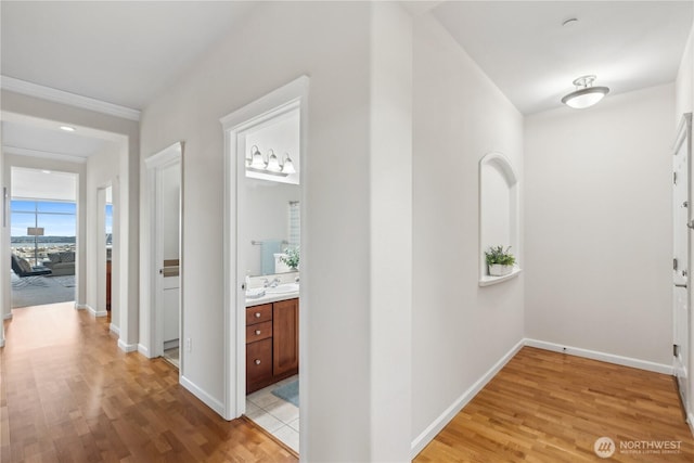 corridor with light wood-style flooring, baseboards, and a sink