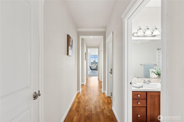 corridor featuring a sink, baseboards, and light wood-style floors