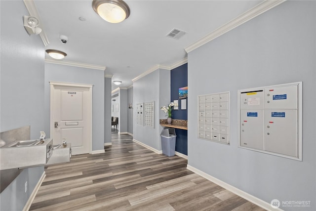 corridor featuring wood finished floors, visible vents, baseboards, mail area, and crown molding