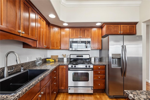 kitchen featuring a sink, dark stone countertops, appliances with stainless steel finishes, crown molding, and light wood finished floors