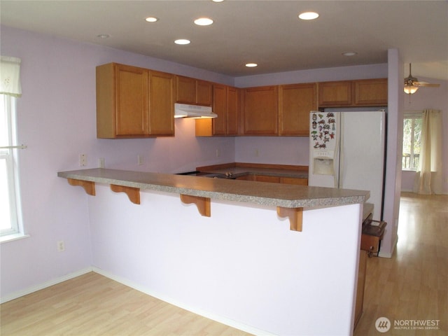 kitchen featuring a breakfast bar, a peninsula, brown cabinets, under cabinet range hood, and light wood-style floors
