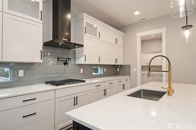 kitchen featuring wall chimney range hood, white cabinetry, visible vents, stainless steel gas stovetop, and a sink
