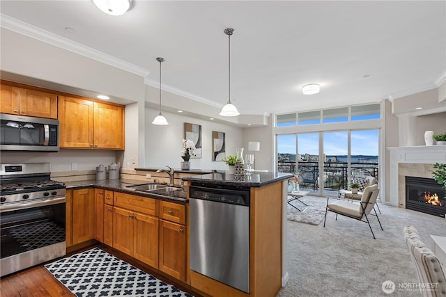 kitchen with dark stone countertops, brown cabinetry, a sink, stainless steel appliances, and crown molding