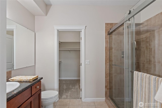 bathroom with toilet, a shower stall, tile patterned flooring, a spacious closet, and vanity