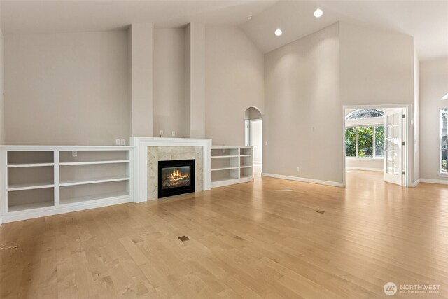 6719 Prairie Ridge Dr NE, Olympia, WA 98516 - unfurnished living room with arched walkways, a tile fireplace, high vaulted ceiling, and light wood-style floors