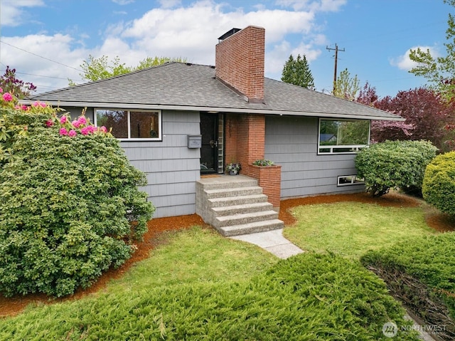back of property with roof with shingles, a chimney, and a yard