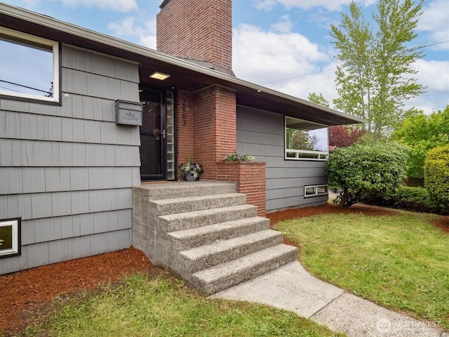 view of exterior entry with a yard and a chimney