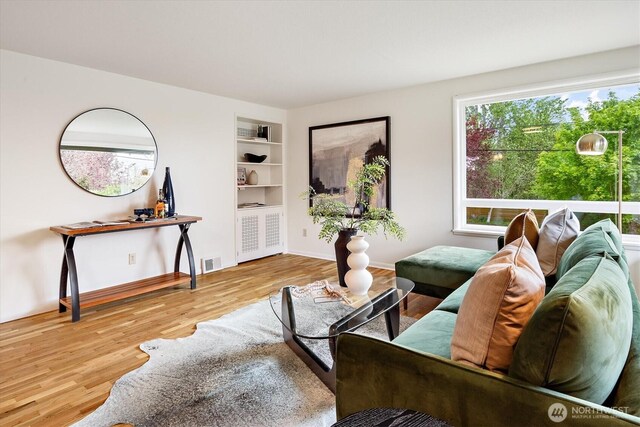 living area featuring visible vents, baseboards, wood finished floors, and built in shelves