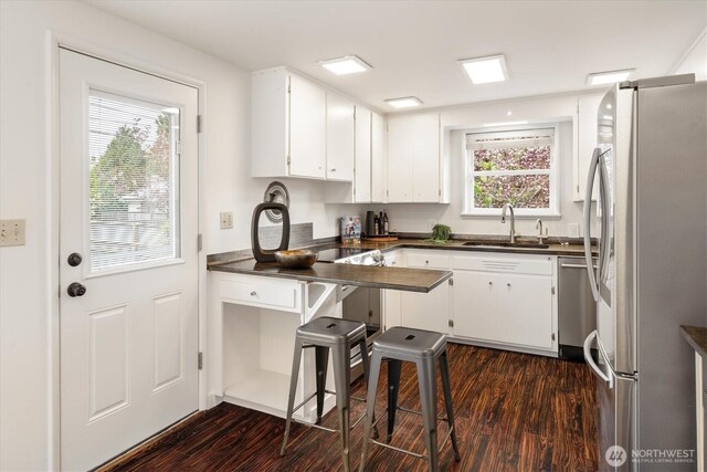 kitchen with appliances with stainless steel finishes, dark countertops, a sink, dark wood-style floors, and white cabinetry