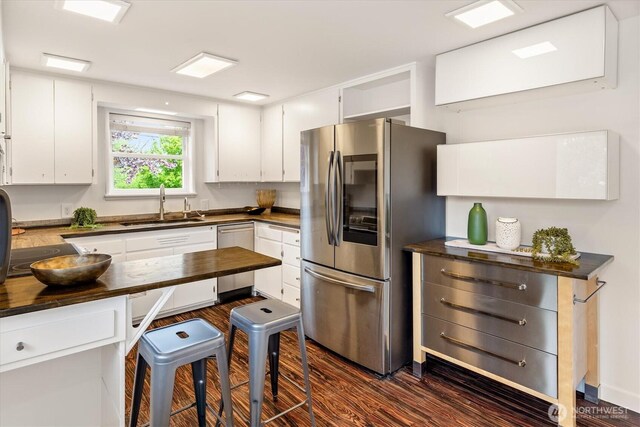 kitchen featuring appliances with stainless steel finishes, dark wood finished floors, a sink, butcher block counters, and white cabinetry