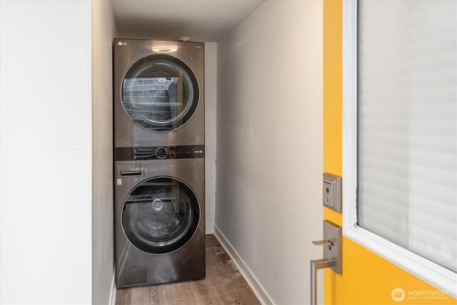 washroom with laundry area, baseboards, stacked washer / drying machine, and wood finished floors
