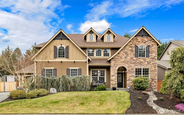 view of front of house with board and batten siding, a shingled roof, a front lawn, fence, and stone siding