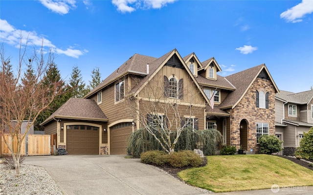 view of front facade featuring a front lawn, stone siding, fence, concrete driveway, and a shingled roof