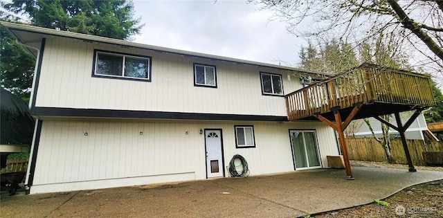 rear view of house with fence, a wooden deck, and a patio