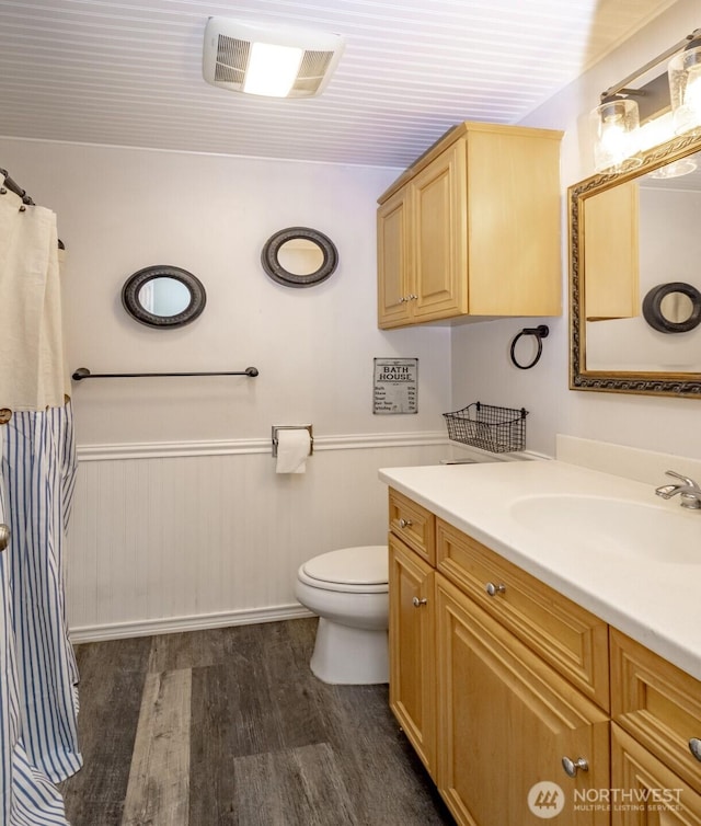 full bath with toilet, vanity, wood finished floors, wainscoting, and visible vents