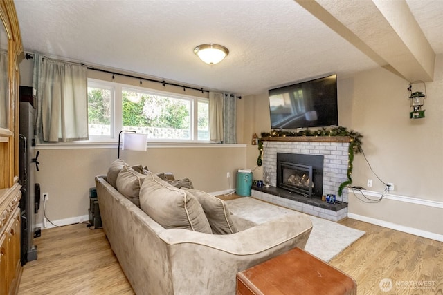 living room with baseboards, a textured ceiling, a fireplace, and light wood-type flooring