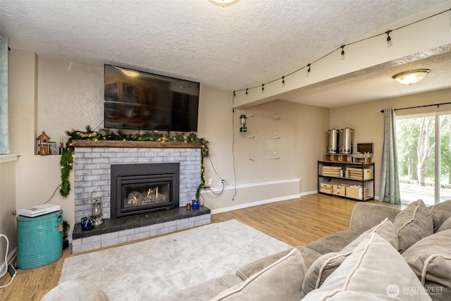 living room with a brick fireplace, wood finished floors, rail lighting, and a textured ceiling
