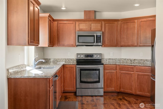 kitchen with brown cabinetry, appliances with stainless steel finishes, light stone countertops, a sink, and dark wood-style floors