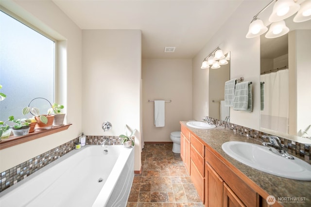 bathroom featuring double vanity, a sink, a bath, and stone tile flooring