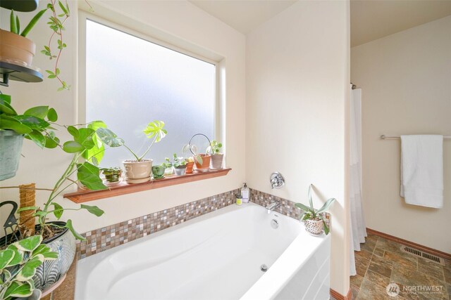bathroom featuring baseboards, a garden tub, stone finish flooring, and visible vents