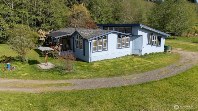 view of side of property with a forest view, roof with shingles, a lawn, and central AC