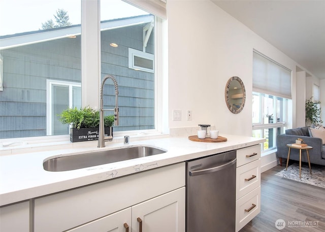 kitchen featuring white cabinets, light stone countertops, a sink, wood finished floors, and stainless steel dishwasher