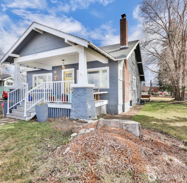 bungalow featuring a porch, a chimney, and a front lawn