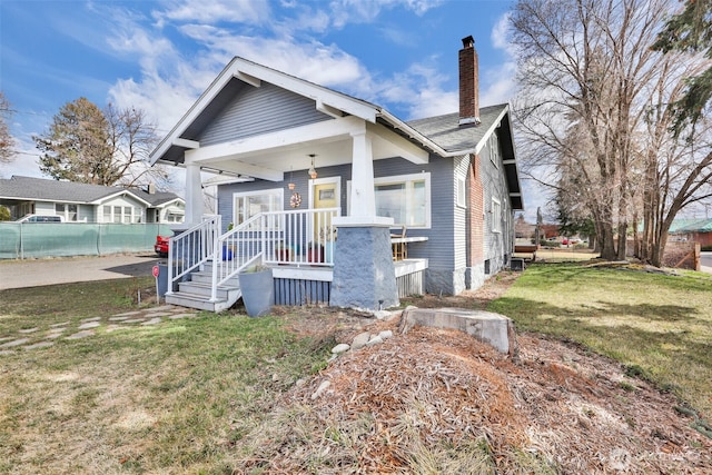 bungalow-style home with fence, a front yard, a porch, and a chimney