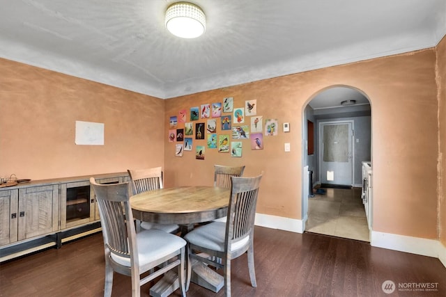 dining space with arched walkways, baseboards, and dark wood finished floors