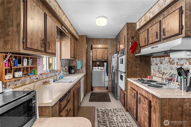 kitchen featuring a sink, under cabinet range hood, appliances with stainless steel finishes, light countertops, and washer / dryer