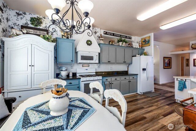 kitchen featuring dark wood finished floors, dark countertops, baseboards, an inviting chandelier, and white appliances