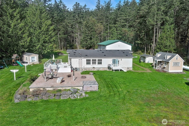 rear view of property featuring a patio, a forest view, a playground, and an outbuilding