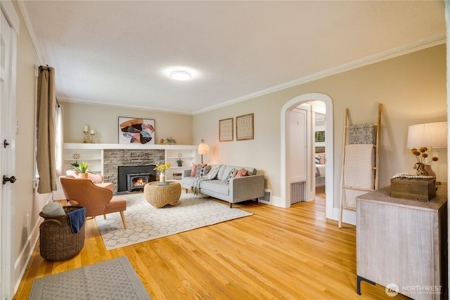 living area with crown molding, baseboards, a fireplace, arched walkways, and light wood-style floors