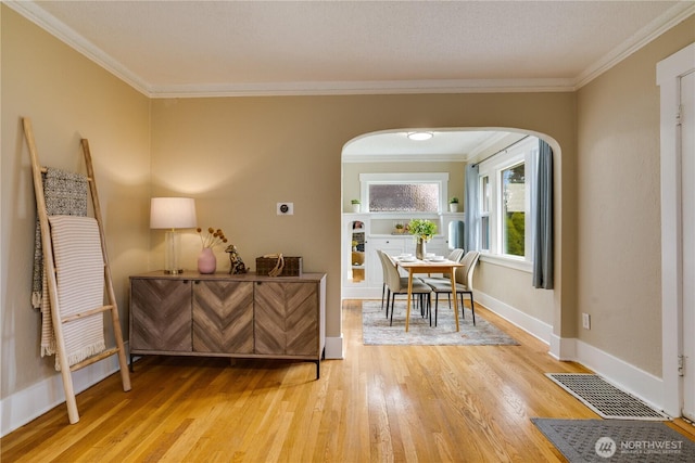 interior space featuring light wood finished floors, baseboards, visible vents, arched walkways, and ornamental molding