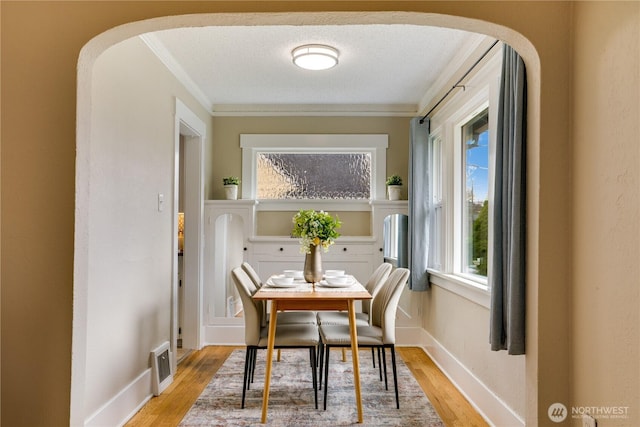 dining room with visible vents, crown molding, light wood-style floors, and arched walkways