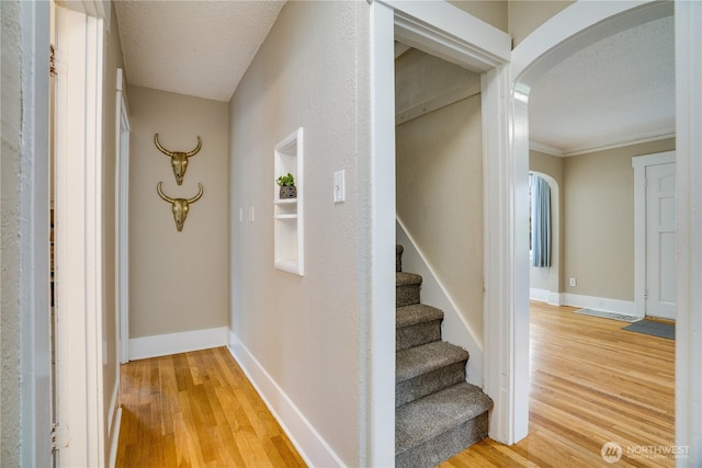 corridor featuring arched walkways, baseboards, and light wood-type flooring