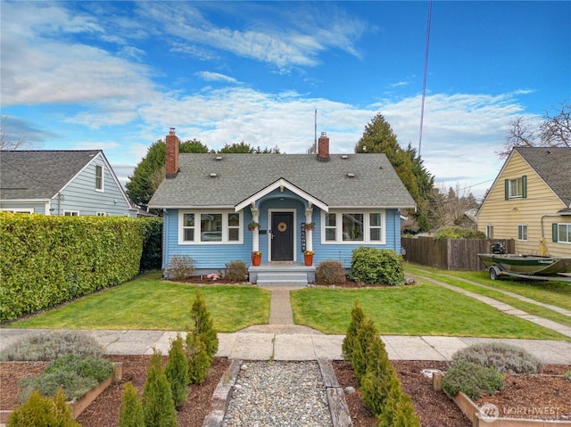 bungalow-style house with a shingled roof, fence, a chimney, and a front yard