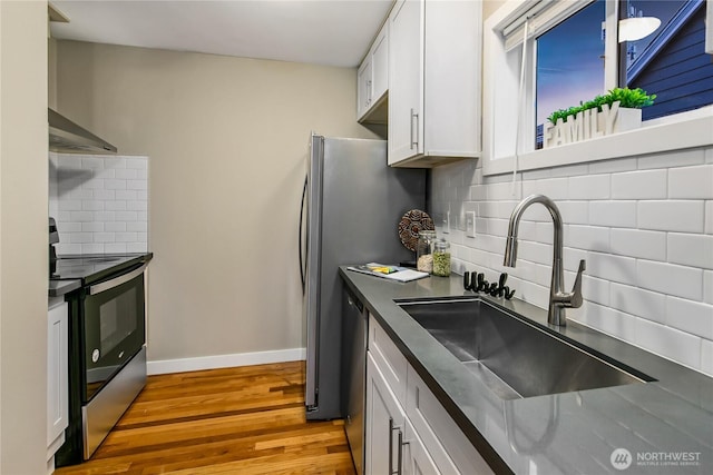 kitchen featuring a sink, dark countertops, white cabinetry, appliances with stainless steel finishes, and wall chimney exhaust hood