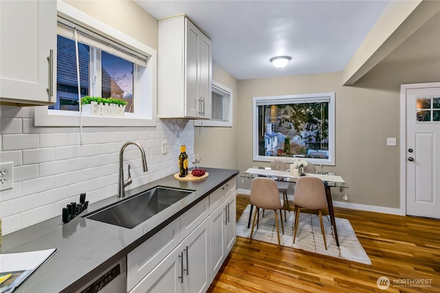 kitchen with a sink, tasteful backsplash, wood finished floors, white cabinetry, and baseboards
