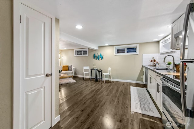 kitchen with dark wood-style floors, baseboards, a sink, white cabinetry, and backsplash
