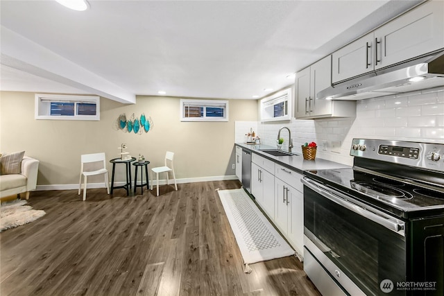 kitchen featuring dark wood-type flooring, under cabinet range hood, decorative backsplash, appliances with stainless steel finishes, and a sink