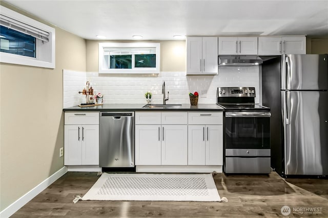 kitchen featuring dark countertops, backsplash, baseboards, stainless steel appliances, and a sink