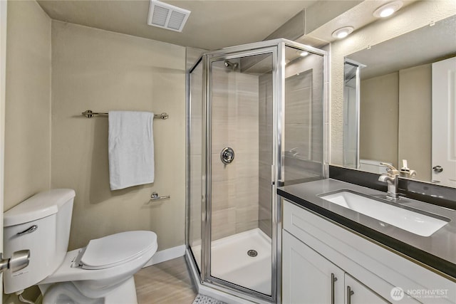 bathroom with visible vents, toilet, a shower stall, baseboards, and vanity