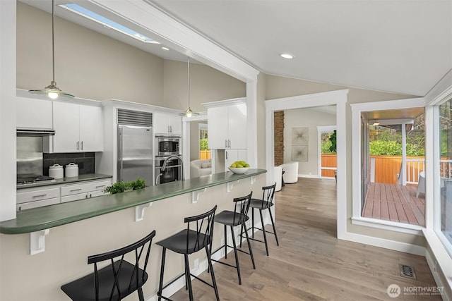 kitchen featuring vaulted ceiling, dark countertops, built in appliances, a breakfast bar area, and backsplash