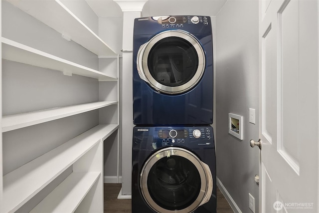 washroom with stacked washer / dryer, laundry area, baseboards, and dark wood-style floors