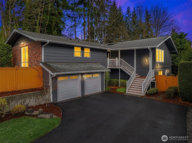 view of front of home with driveway, stairs, a garage, fence, and a shingled roof
