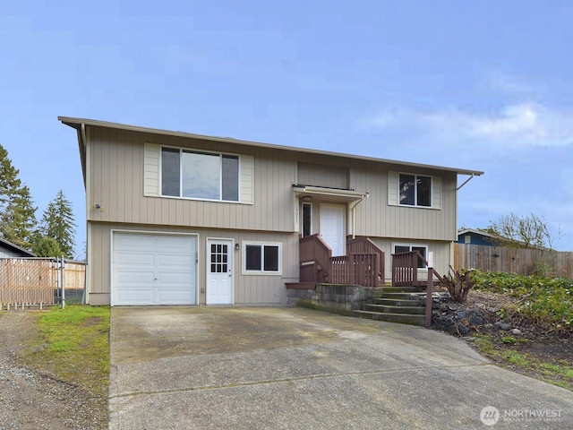 split foyer home featuring concrete driveway, an attached garage, and fence