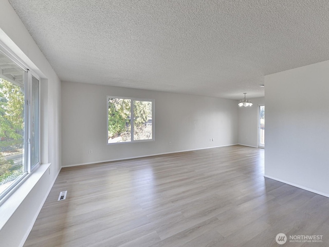 unfurnished room featuring a wealth of natural light, visible vents, wood finished floors, and a chandelier