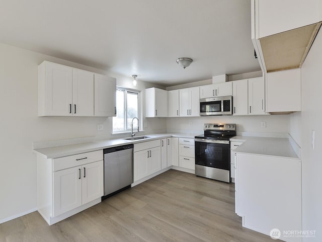 kitchen with light wood finished floors, a sink, white cabinetry, appliances with stainless steel finishes, and light countertops