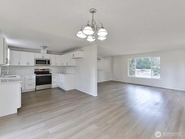kitchen with light wood finished floors, an inviting chandelier, a sink, stainless steel appliances, and open floor plan
